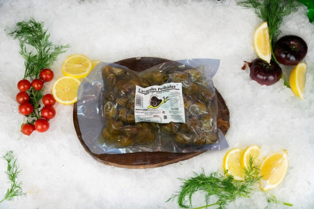 Bolsa al vacío de 1 kg de caracoles precocidos Bobe G Caracoles Peribáñez sobre tabla rústica y lecho de hielo en set oficial de Puerto Cabrera