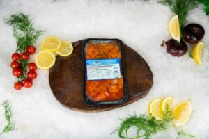 Bandeja termosellada de 500 g de cazón en adobo caella sobre tabla rústica y lecho de hielo en set oficial de Puerto Cabrera